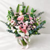 Pastel pink and white flower arrangement with roses and eucalyptus in a round glass vase with pink ribbon, angled view