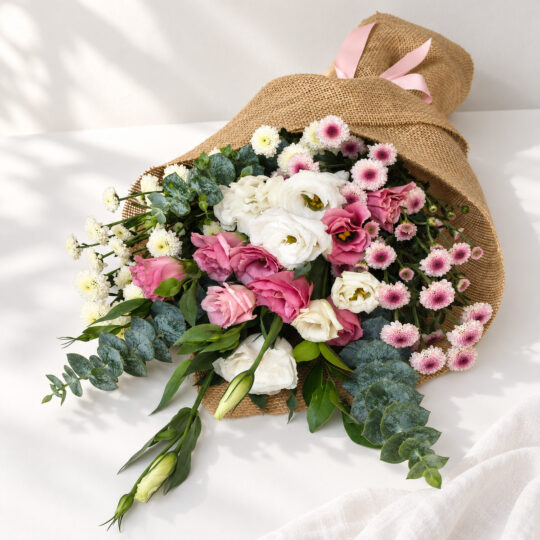 White and pink lisianthus stems with calimero chrysanthemums in jute wrap lying flat, angled view
