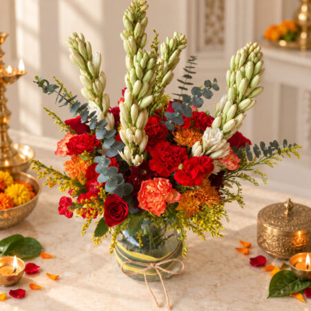 Tuberose, red carnation and orange chrysanthemum arrangement in a leaf-wrapped glass vase, close angled view
