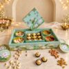 Open mint and gold lotus-print gift box with round tins of pistachios, cashews, almonds and raisins around a tray of Ferrero Rocher, angled view