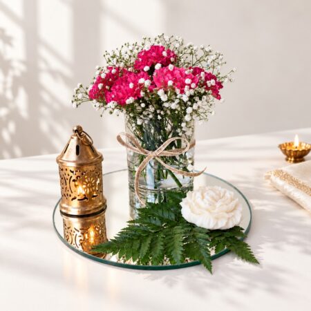 Diwali carnation centrepiece in Bangalore with dark pink carnations and baby’s breath in a glass vase on a mirror base with lantern and rose candle