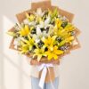 Person holding the Bright Side bouquet of yellow and white lilies in a jute wrap with a white satin bow