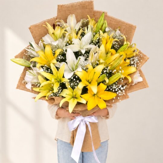 Person holding the Bright Side bouquet of yellow and white lilies in a jute wrap with a white satin bow