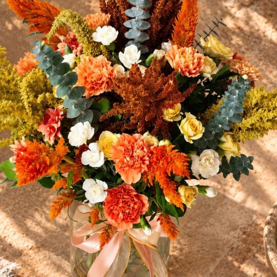 Sunset-coloured flower arrangement in a glass jar vase with ribbon, top view