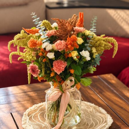Orange, peach and white flower arrangement with eucalyptus and amaranthus plumes in a glass jar vase, front view