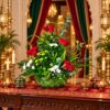 Tall red rose centrepiece with green chrysanthemums, ferns and looping grass in a handwoven basket, front view