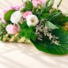 Close-up of white eustoma, pink spray carnations, a pink rose, limonium and a hydrangea leaf on a woven coconut leaf base