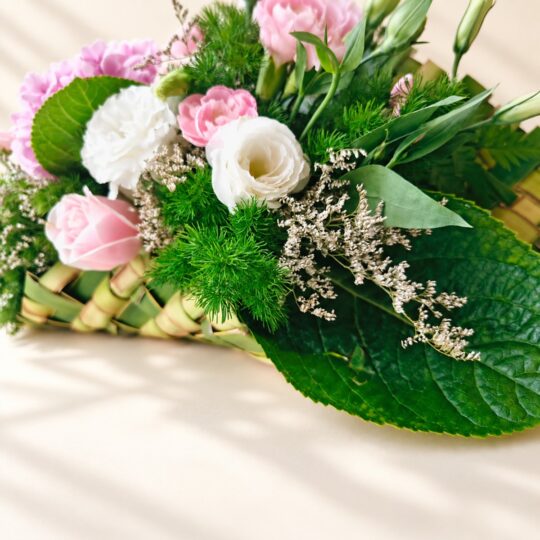 Close-up of white eustoma, pink spray carnations, a pink rose, limonium and a hydrangea leaf on a woven coconut leaf base