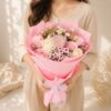 Pink and white mixed flower bouquet held in hand, wrapped in pink paper with a cloth ribbon