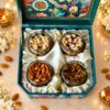 Top view of cashews, pistachios, almonds and golden raisins in four glass jars on cream satin inside a teal gift box