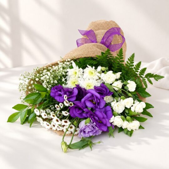 Purple lisianthus and white carnation stems with baby's breath in jute wrap lying flat, angled view