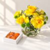 Diwali yellow roses gift in Bangalore with yellow roses and button chrysanthemums in a glass fishbowl vase and a box of laddoo candles