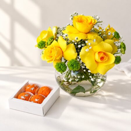Diwali yellow roses gift in Bangalore with yellow roses and button chrysanthemums in a glass fishbowl vase and a box of laddoo candles