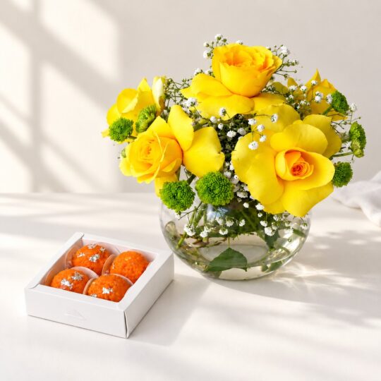 Diwali yellow roses gift in Bangalore with yellow roses and button chrysanthemums in a glass fishbowl vase and a box of laddoo candles