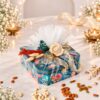 Front view of the open gift box with the cork fairy light draped around the four glass jars of dry fruits, lighting up the satin lining. The printed jar lids are placed on either side.